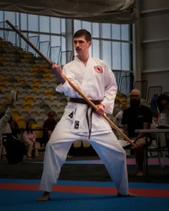 Hayden Hosking in his gi and brown belt, in stance with a bo at a tournament