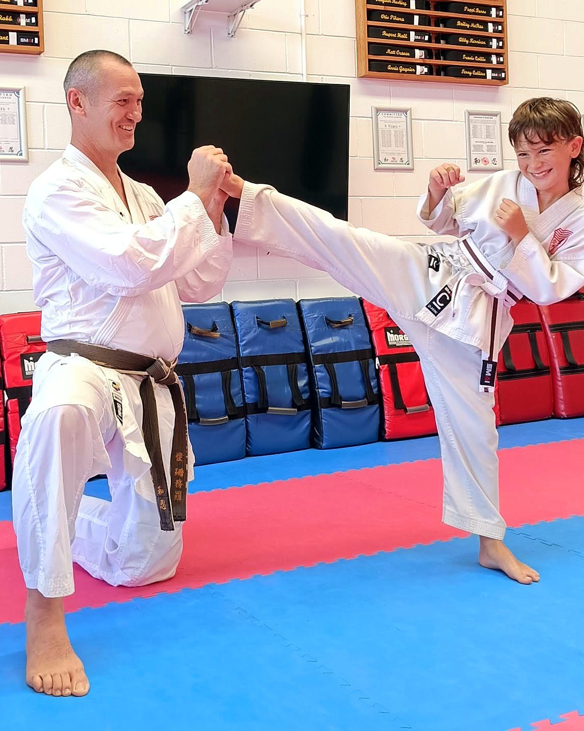 Sensei Martin kneeling to hold a student's kick, both smiling